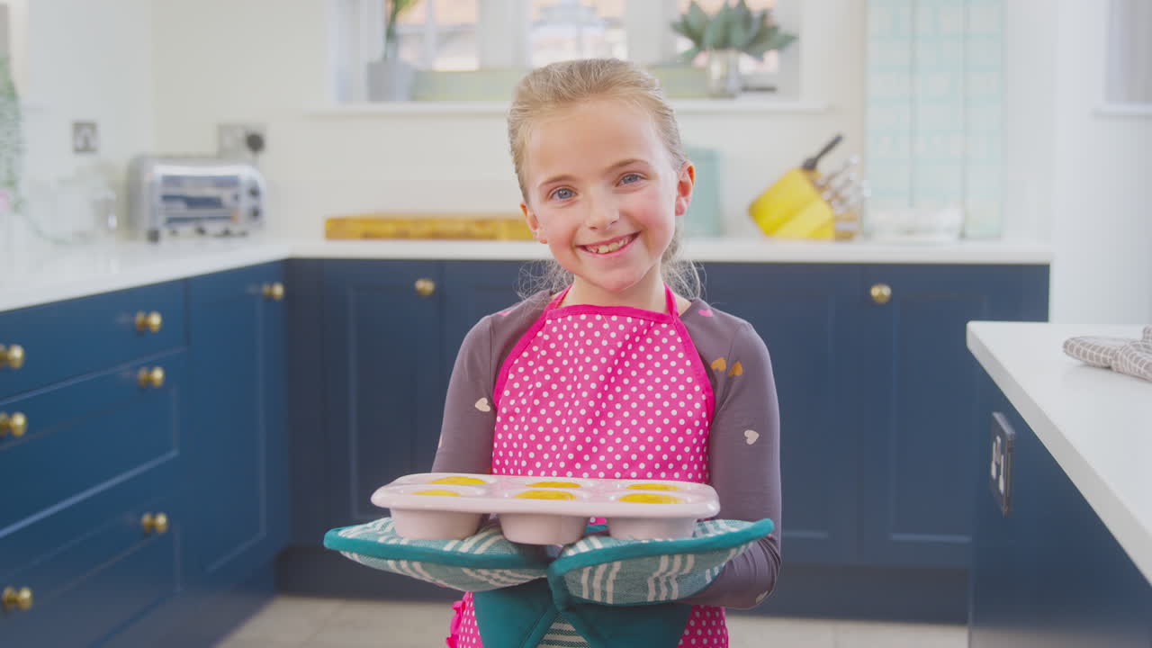 Ritratto di ragazza nella cucina di casa che tiene un vassoio di cupcake appena sfornati, con un'espressione orgogliosa.