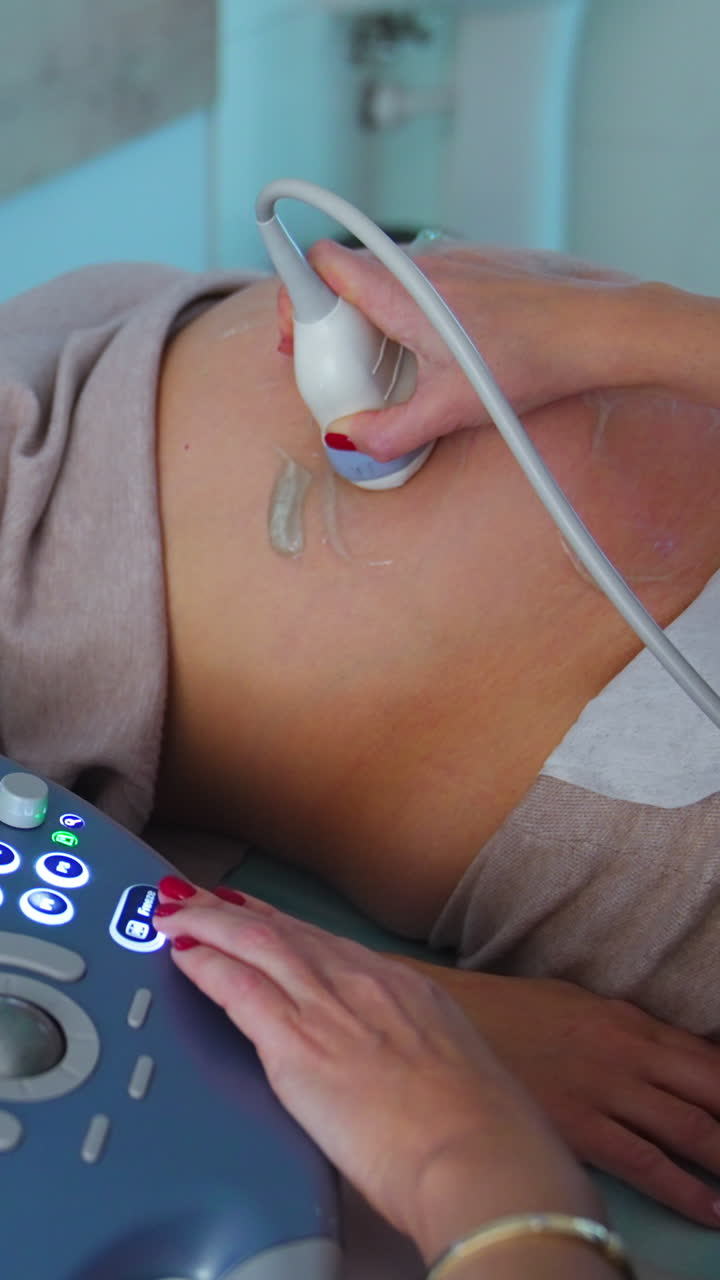 Woman in mask lies on the couch for ultrasound check up. Keyboard of ultrasonic equipment at foreground close up. Vertical video
