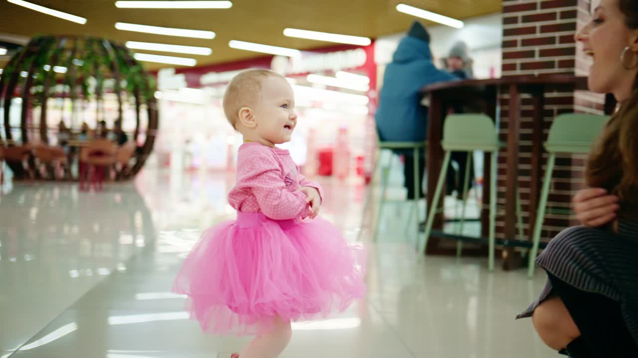 Adorabile bambina in vestito tutù rosa che sorride e indica in un centro commerciale