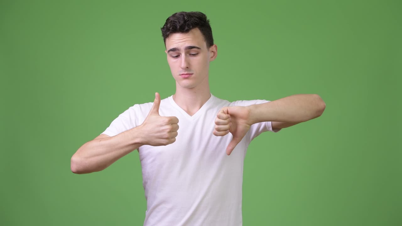 Young handsome man choosing between thumbs up and thumbs down