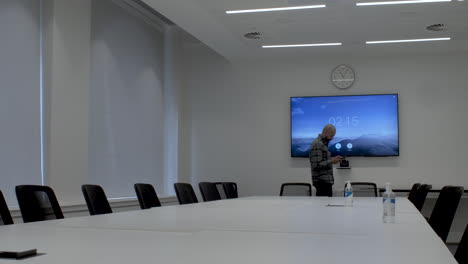 an asian office employee pacing around an empty boardroom while texting on his mobile phone, the man focused on his screen and oblivious to his surroundings