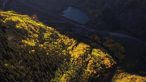 Fall-Season-in-Countryside-of-Colorado-USA,-Drone-Shot-of-Yellow-Green-Forest-Above-State-Road-and-Lake