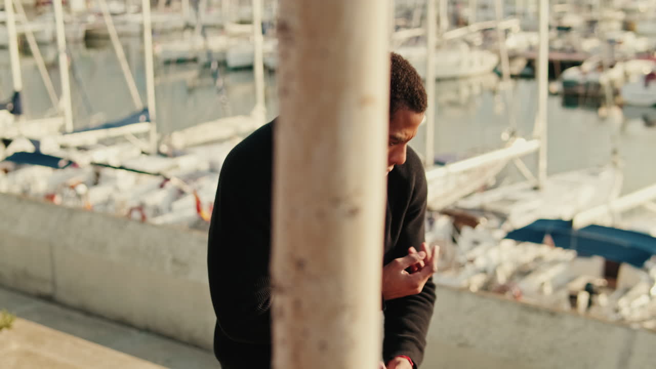 Thoughtful Young Man Stretching by Boats in a Sunny Marina