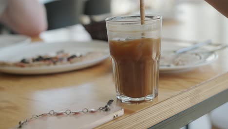 female hand stirring iced coffee in cafe