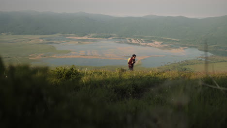 hiker with a green backpack and sunglasses walking uphill on grassy terrain