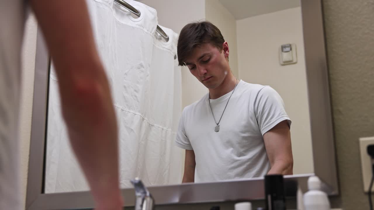 젊은 근육  ⁇ 색 남성이 거울 반사에서 호텔 욕실에서 이빨을  ⁇ 고 있습니다.