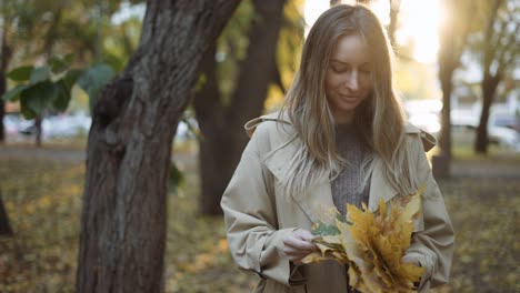 thoughtful woman with pile of golden leaves in hands in sunny autumn park