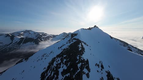 fpv drone footage gliding above the summits and diving down steep mountain slopes above the clouds during the mesmeriszing midnight sun in northern norway