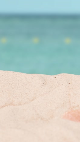 Vertical-Video-Summer-Holiday-Concept-Of-Sunglasses-Book-Beach-Towel-On-Sand-Against-Sea-Background