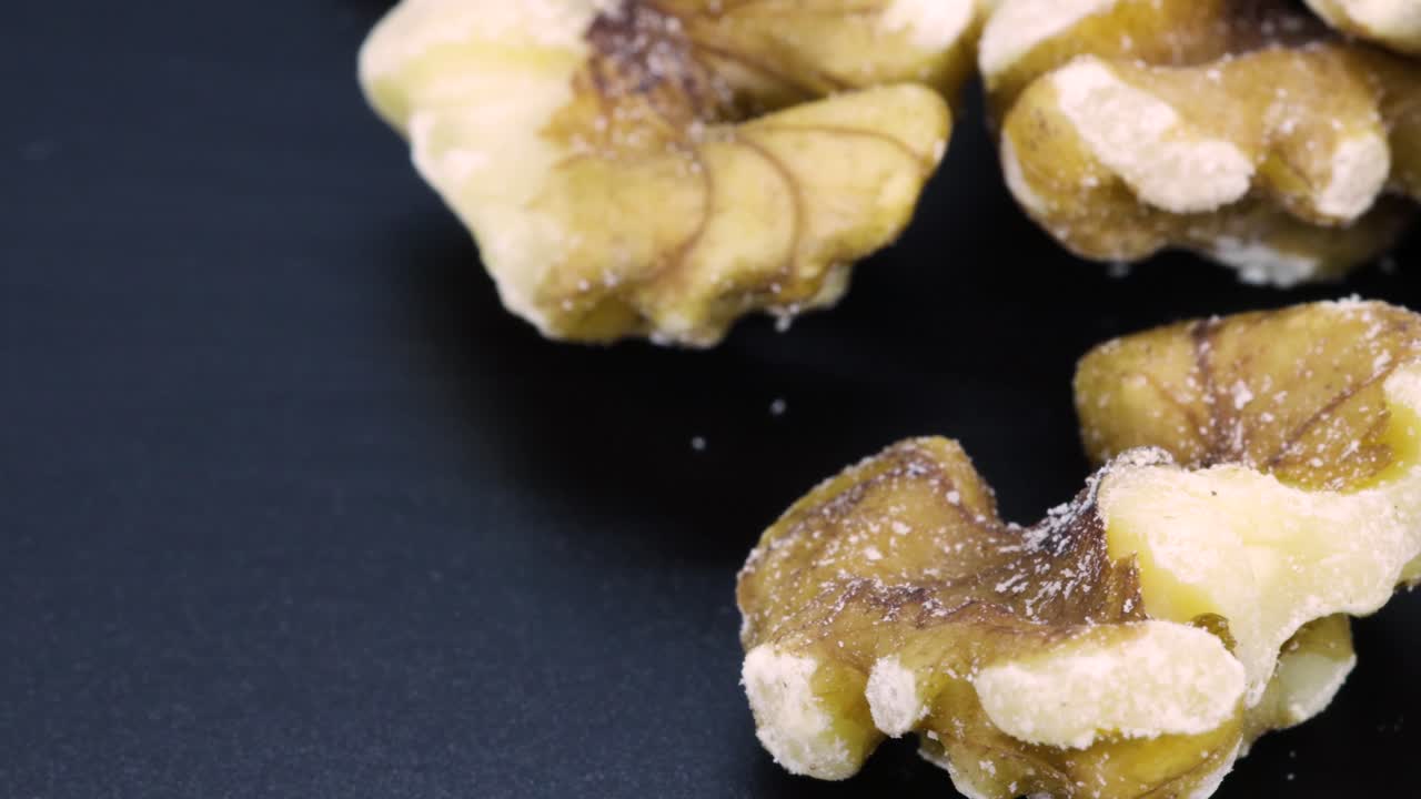 Extreme close up view of walnuts over a black surface on the right side of the frame, macro shot in 4k