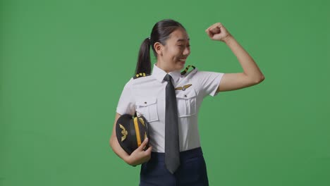 una mujer piloto asiática sonriendo y flexionando su bíceps mientras está de pie en el estudio de fondo de la pantalla verde