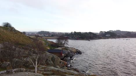 panoramic view of waves hitting small cottage on rocky cliff, sweden