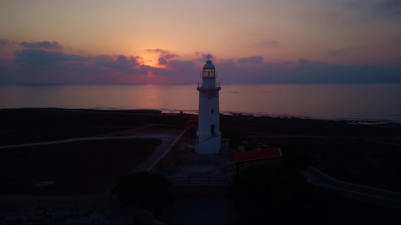 Faro iconico si erge contro un drammatico cielo al tramonto con nuvole che si riflettono sull'oceano tranquillo