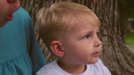 a close-up of a smiling little boy with traces of cake on his mouth, while a partial view of a woman, possibly his mother, watches him with affection