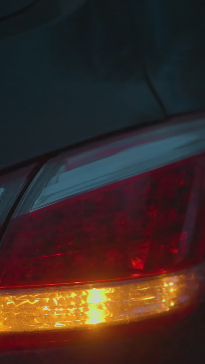 primer plano de la luz trasera de un coche y la señal de giro iluminada en la oscuridad, creando una atmósfera borrosa y de mal humor, las luces rojas y ámbar contrastan contra el fondo oscuro