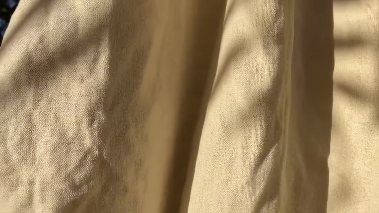 Video ravvicinato di tessuto beige con ombre della luce solare, che cattura la texture e il movimento