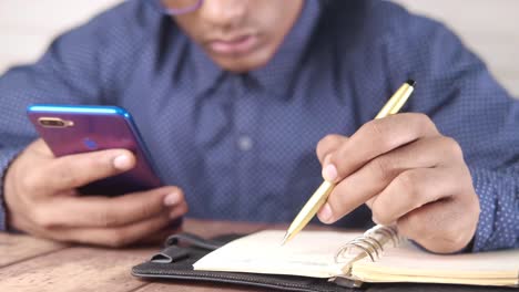 man using smartphone and writing in a notebook