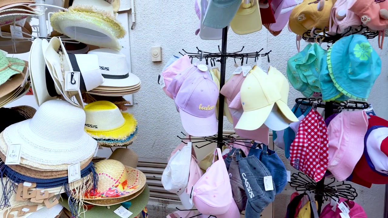Una panoramica rivela cappelli di paglia colorati, borse tote e abbigliamento da spiaggia in un mercato francese.
