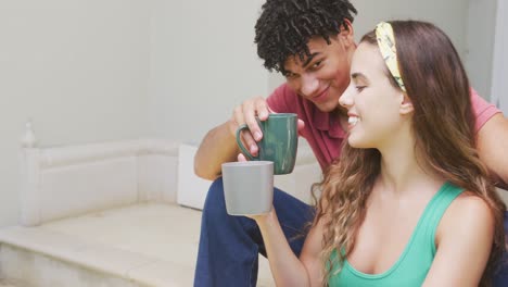 happy biracial couple spending time at home drinking coffee and sitting on stairs