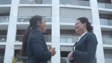 happy female business colleagues meeting at office building, giving high five and discussing successful project or contract