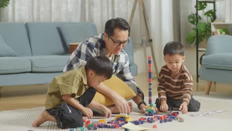 full body of asian father and sons assemble the construction set colorful plastic toy brick on a mat at home