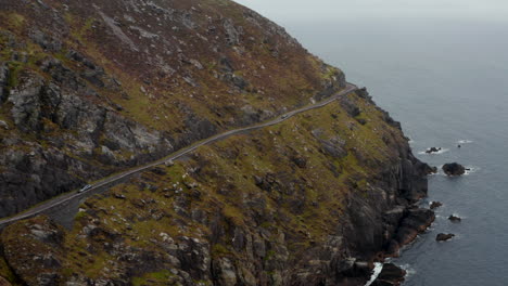 Breath-taking-shot-of-slowly-moving-car-on-narrow-panoramic-route-in-steep-slope-above-sea-coast.-Dangerous-road-around-Slea-Head.-Ireland