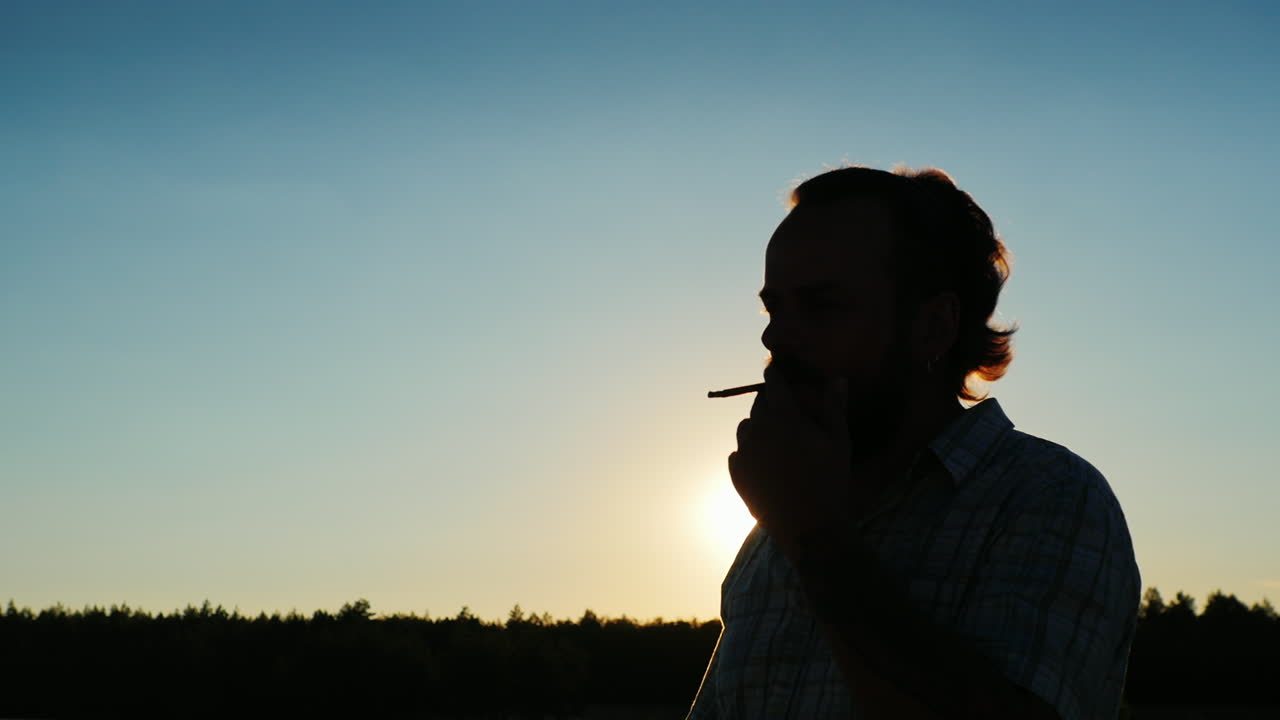 silhouette d'un homme barbu qui fume au coucher du soleil