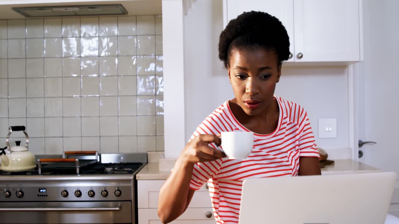 mujer usando una computadora portátil mientras toma café en la cocina