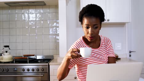 Woman-using-laptop-while-having-coffee-in-kitchen