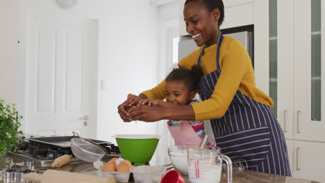 Happy-african-american-mother-and-daughter-wearing-aprons-having-fun-while-cooking-in-kitchen