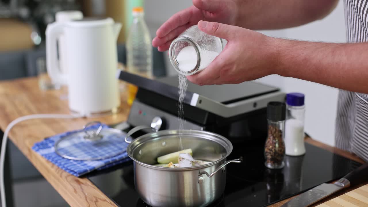 Person adding seasoning to vegetables in a pot