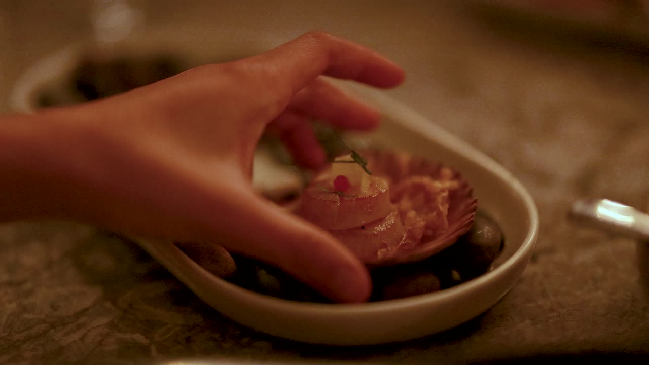 A hand delicately places grilled scallops on a decorative plate. Warm lighting creates an inviting and sophisticated dining atmosphere