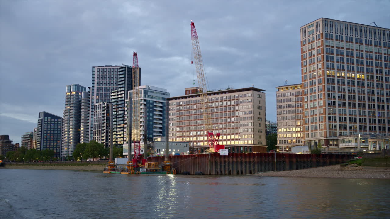 View of London from a floating boat on the Thames River at sunset, United Kingdom. Modern residential buildings located on the embankment street along the river