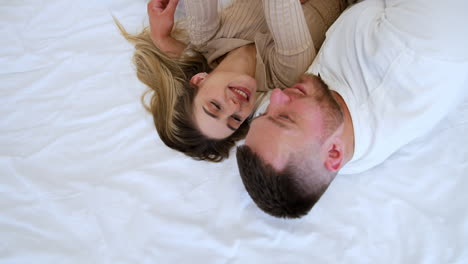 caucasian man and woman lie on the bed hugging. blonde girl is holding her phone taking selfie. top view.
