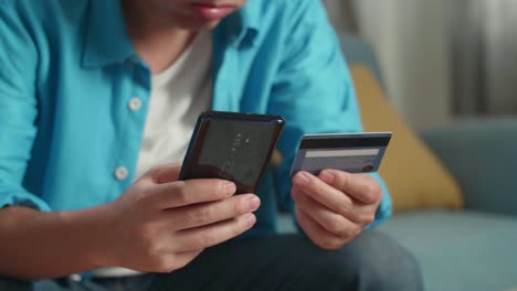 un hombre con una tarjeta de crédito y un teléfono inteligente sacudiendo la cabeza debido a no poder pagar dinero