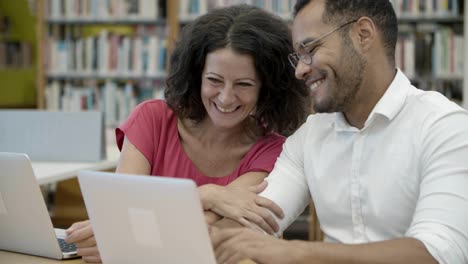 cheerful colleagues sitting at library and communicating