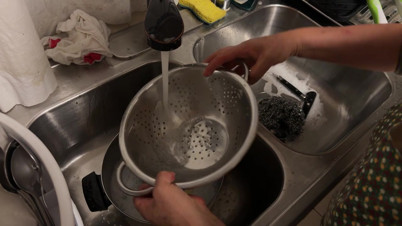 En kvinde vasker brugt service i hånden i en køkkenvask, mens hun rengør tallerkener og køkkengrej efter madservering.
