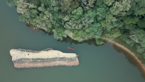kayak en un lago tranquilo entre una roca y el borde del bosque