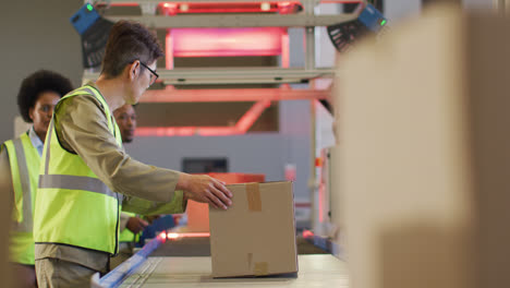 diverse male and female workers wearing safety suits with boxes on conveyor belt in warehouse