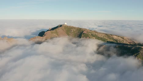 clouds surrounding mountain with weather station on top in madeira, aerial