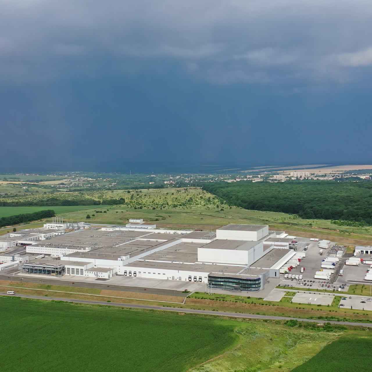 Birds-eye view to the modern industrial buildings. Large manufacturing plant under the blue sky among green nature. Camera moves right.