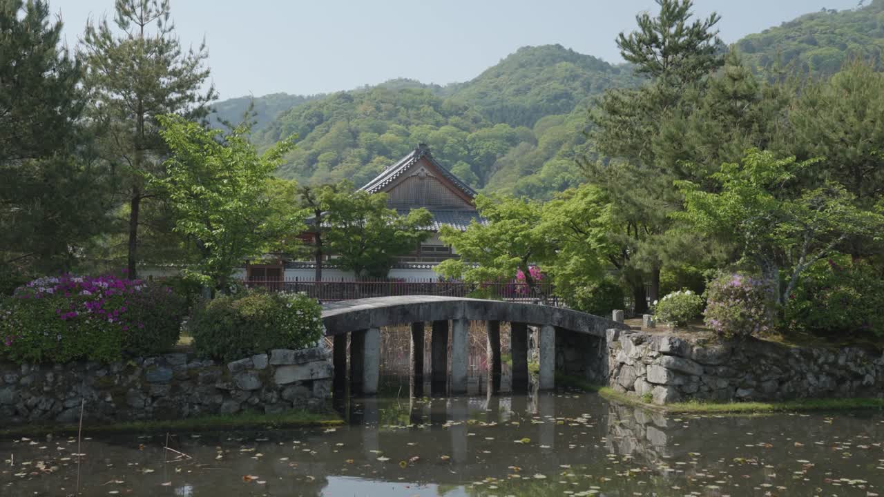 Japonský kamenný most přes vodu a tradiční japonský dům v přírodě za slunného letního dne v Kjótu, Japonsko