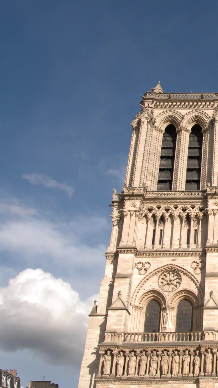 Mavi bir gökyüzü altında Notre Dame Katedrali'nin süslü Gotik mimarisinin alçak açıdan görünümü.