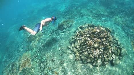 underwater shot following a man swimming around a rock formation at the bottom of the ocean