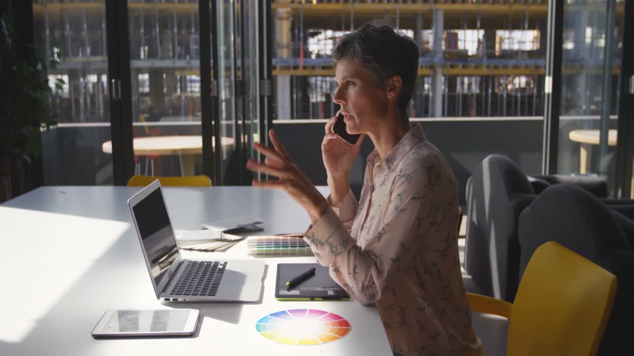 Female graphic designer talking on mobile phone at desk 4k