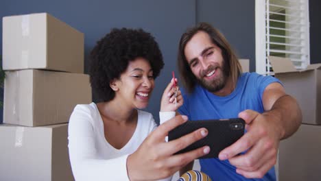 Mixed-race-couple-holding-keys-on-video-call-on-smartphone-at-new-apartment-house