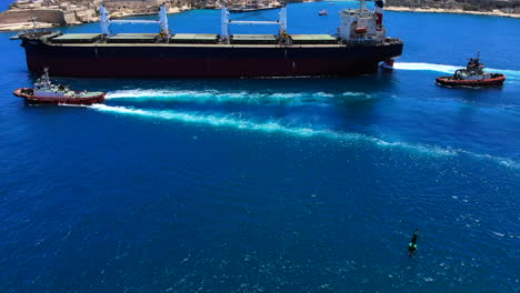 un perfil aéreo estable de un buque de carga gigante que sale del puerto de valletta, malta, con la ayuda de tres remolcadores