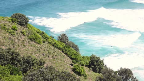 green hillside with waves crashing against the shore