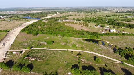 Moving-slowly-towards-abandoned-farm-out-buildings,-with-a-new-road-under-construction-o-the-left-and-a-soil-conservation-reservoir-in-the-distance