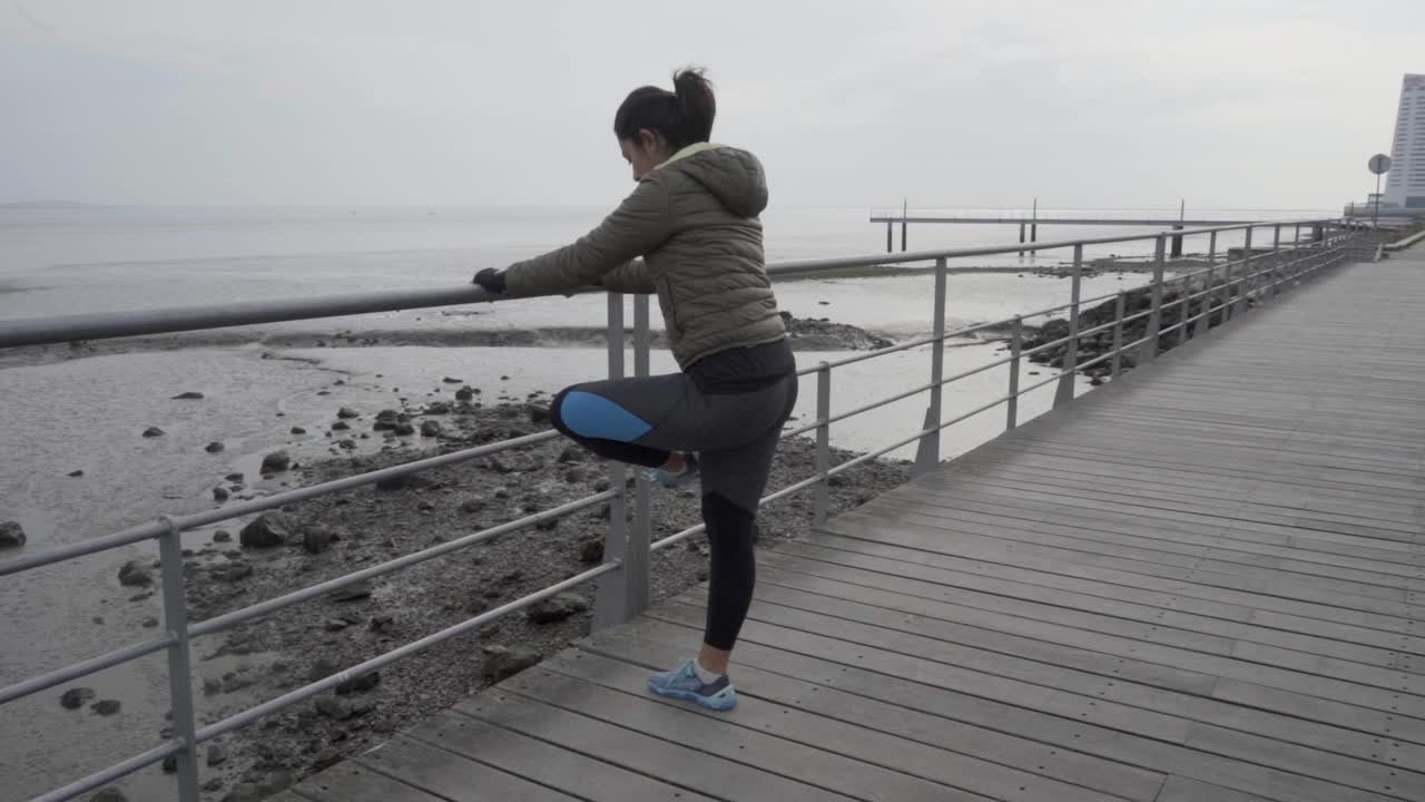 Concentrated young hindu woman warming up near metal railings on wooden pier